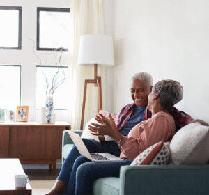 Elderly african american couple talking, smiling and looking at a laptop, while sitting on the couch