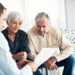 Man, out of focus in foreground, is showing a pile of paperwork to an elderly couple